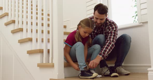 Father helping her daughter to wear shoes on stairs in a comfortable home 4k