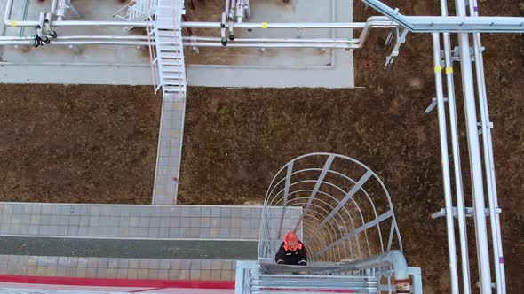 An Oil and Gas Worker Climbs a Metal Ladder to the Roof for Inspection