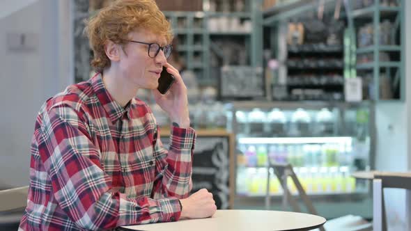 Cheerful Young Redhead Man Talking on Smartphone in Cafe