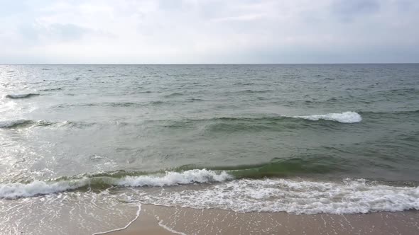 AERIAL: Locked Shot of Beach Over the Dark Waving Sea with Cloudy Sky in the Background