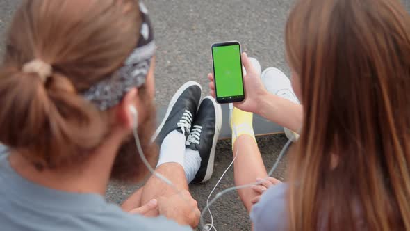 Hipster Young Millennial Friends Sitting Outside and Looking a Green Screen Phone in Park