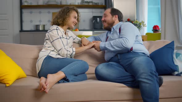 Happy Young Obese Man Holding Attractive Woman Hands on Couch and Talking