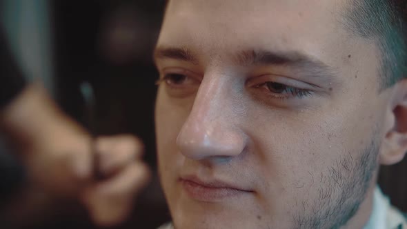 Young Man Sits in a Barber Shop He is Made Up with a Beard Closeup Slow Motion