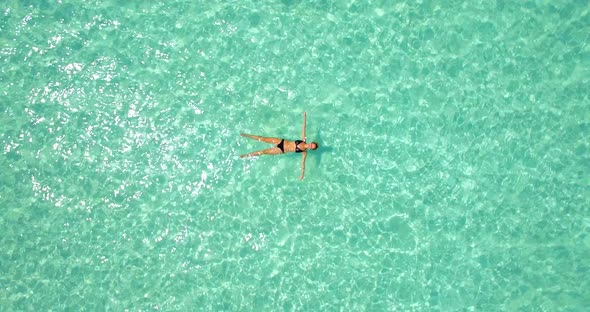 Aerial drone view of a woman floating and swimming on a tropical island.