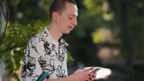 A side view of a hipster man with earrings typing message using hphone