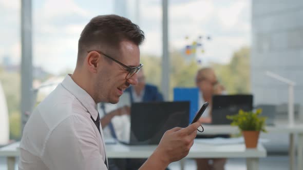 Smiling Young Man Using Smartphone Working in Modern Office