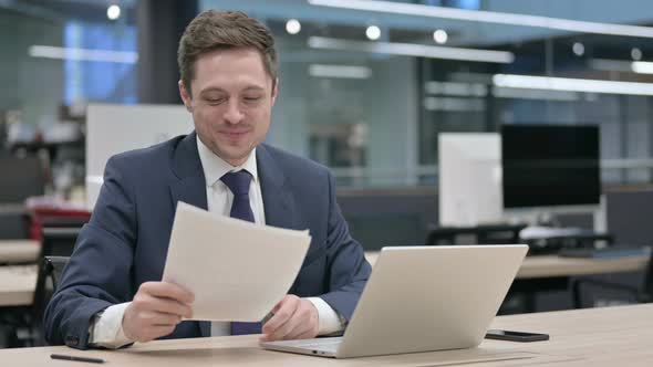 Businessman with Laptop Having Loss While Reading Documents