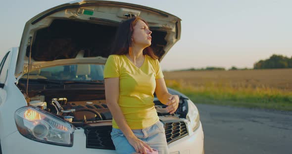 Sad Girl Stands Near Car with Open Hood on Side of Road