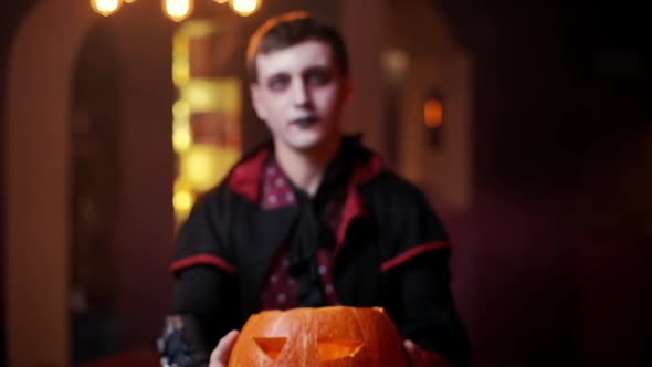 Young Man in a Halloween Costume of Count Dracula Raises a Carved Pumpkin