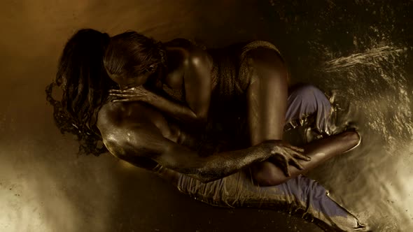 a Woman and a Man with Gold Paint on Their Bodies Embrace While Lying in the Water