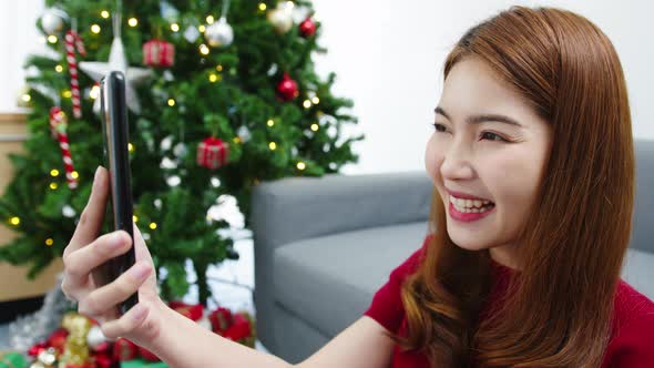 Young Asian female using smart phone video call talking with couple with X'Mas present box