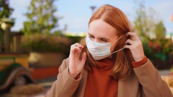 A Woman in a Coat Wears a Protective Medical Disposable Mask While Standing