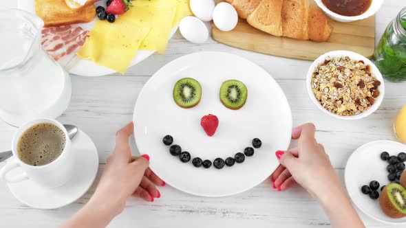 POV Shot Female Hand Having Fun Playing with Smiling Fruit Berry Face on Plate Top View