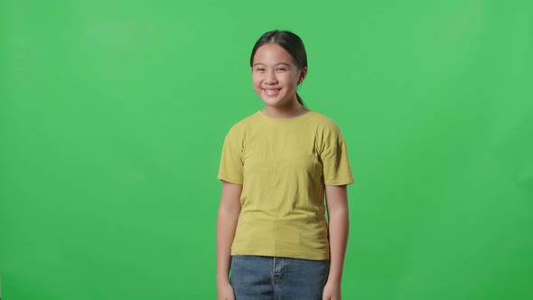 Smiling Young Asian Kid Girl Positively Shaking Her Head At The Camera In The Green Screen Studio