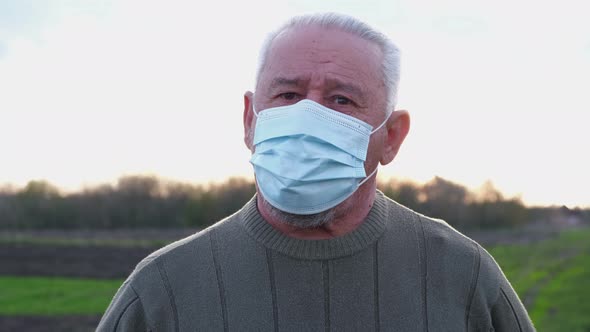 An Elderly Man in a Medical Mask Looks at the Camera