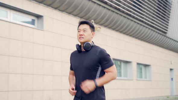 young asian man runner running down the street on urban background of city and park 