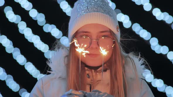 Sparklers in the Hands of a Girl in Mittens Against the Background of the City's Christmas Lights