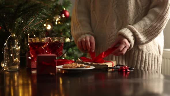 Woman in sweater is wrapping a Christmas gift on a table