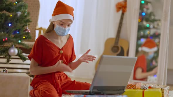 Charming Teenage Girl in Red Pajamas and Christmas Hat Wearing Covid19 Face Mask Talking
