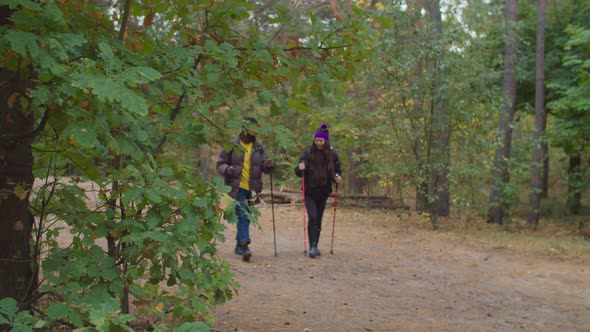 Multiethnic Couple with Trekking Poles Hiking in Wood