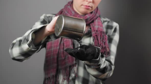 A homeless woman pours coins out of a steel cup and counts them with sadness