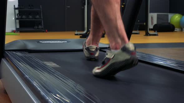 A Fit Man Walks on a Treadmill in a Gym - Closeup on the Feet From Behind