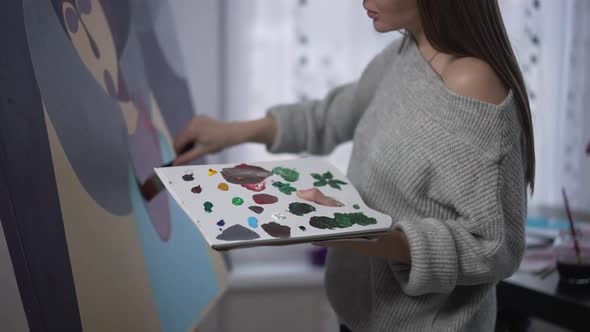 Painting Palette with Acrylic Paints in Hand of Unrecognizable Young Woman Making Strokes on Canvas