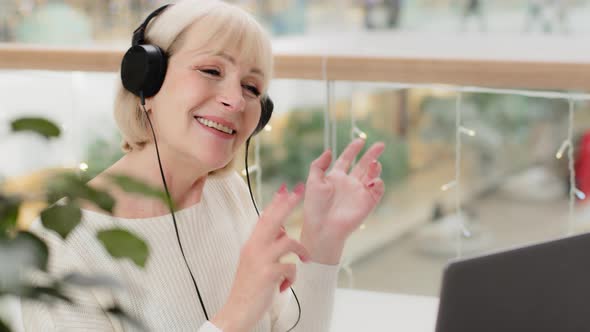 Mature Happy Funny Woman Listening Music with Headphones Sitting at Laptop Joyfully Dancing Cheerful