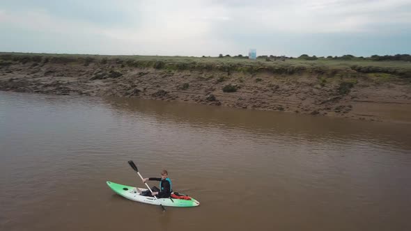 Man kayaking on meandering river, drone pans round kayaker.