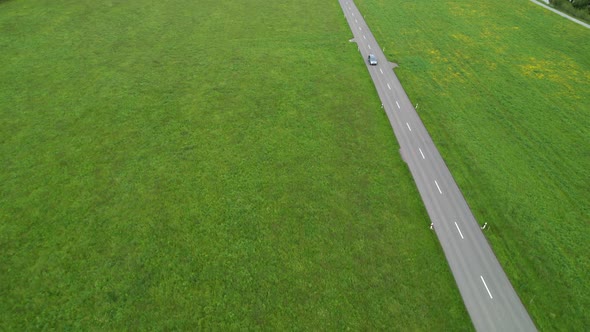 Lonely car drives on a straight street in a green meadow, copy space, aerial.