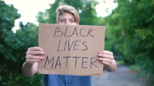 Young Teenager Male Caucasian Ethnicity Blue Shirt Holds Cardboard Box with Handwritten Text BLACK