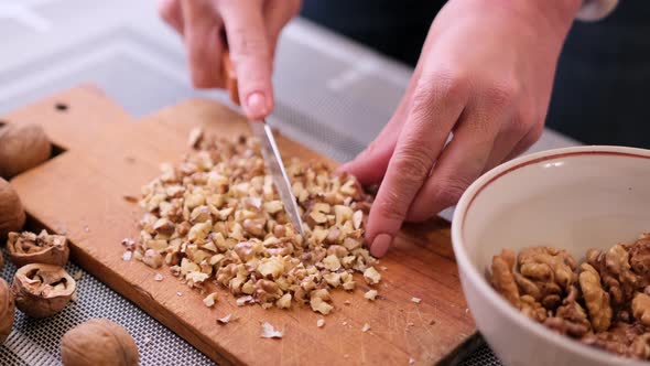 Chopping Walnuts Cores with Kitchen Knife on a Wood Cutting Board