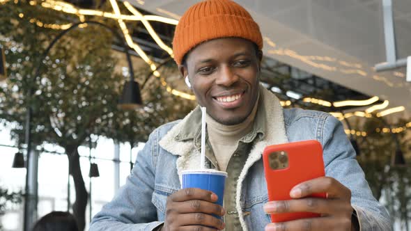 Black Guy with Wireless Headphones Looks Into Smartphone