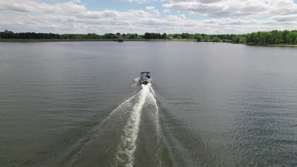 Aerial drone shot over white motor boat speeding over lake water on a cloudy day.