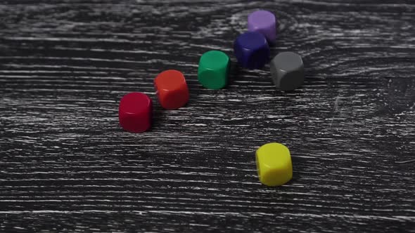 Seven multi-colored game dice fall on an old textured wooden table. 