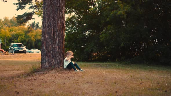 Young Girl Eats Yogurt with Large Spoon Sitting at Tree