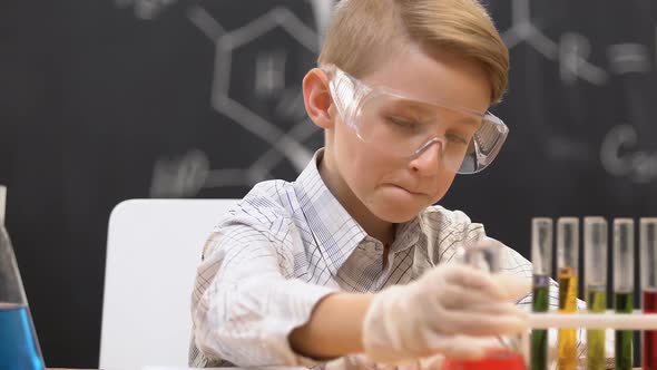 Schoolboy Looking at Flask With Red Liquid, Writing Reaction Data in Copy-Book