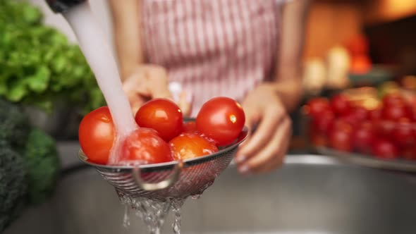 Female Hands Washing a Tomatos Under a Stream of Water at the Kitchen