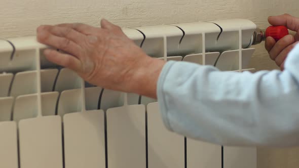 The concept of lonely old age, lack of family warmth. An elderly man touches a scrap heating radiato