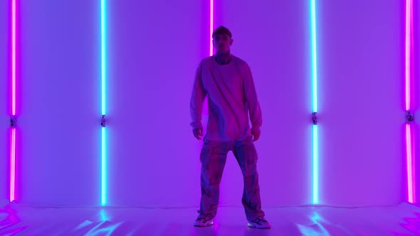 Stylish Young Man with Tattoos Performs Cool Street Dance Against Backdrop of Bright Neon Lights