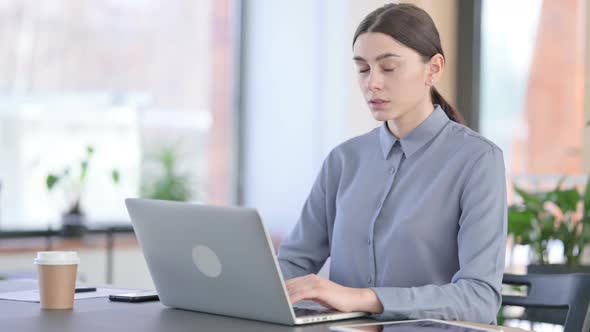 Young Latin Woman Looking at Camera While Working on Laptop