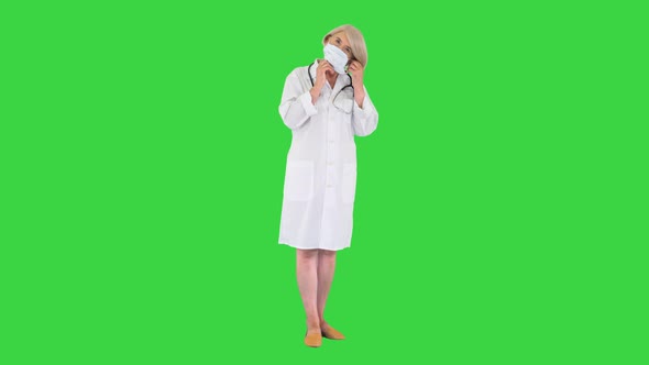 Senior Woman Doctor Putting on Medical Mask Looking at the Camera on a Green Screen, Chroma Key.