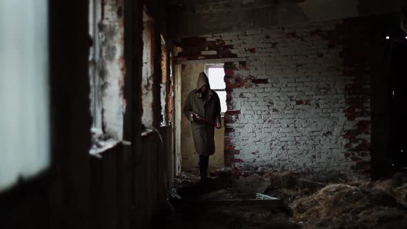 Silhouette of Man in Dark Cloak Walking Through Abandoned Building with an Ax