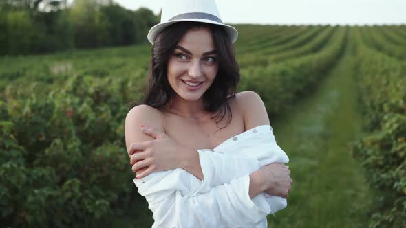 Portrait of Happy Brunette in Hat Smiles and Poses at Camera in Field