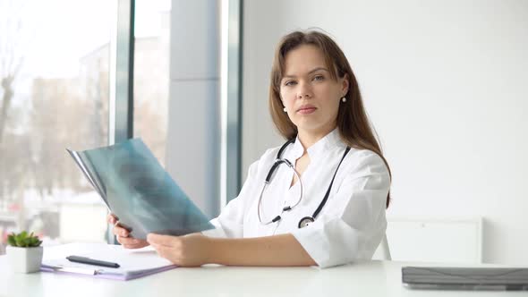 Young Caucasian Woman Doctor Wearing White Medical Coat and Stethoscope Holds the Xray