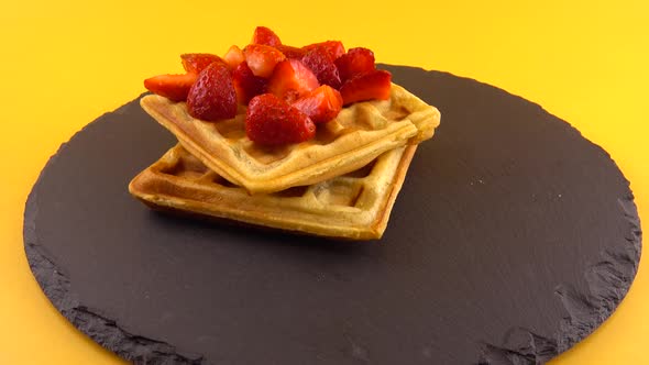 Belgian waffles with strawberry on a stone board on an orange background.