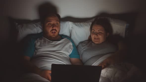 Cheerful Young Obese Couple in Bed in Front of Laptop Watching Movie at Night