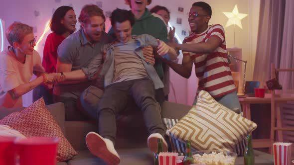 Friends Pulling Man from Couch and Dancing Together at Home Party