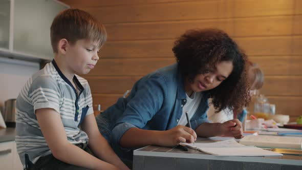 Smart Babysitter Helping Kids Brother and Sister with Homework Writing and Explaining in Apartment