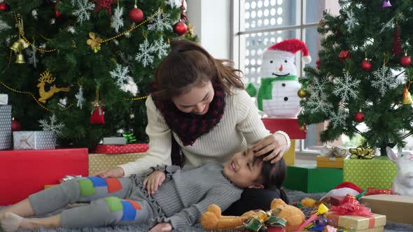 Llittle Asian daughter lays on mother's lap and mother kisses her forehead